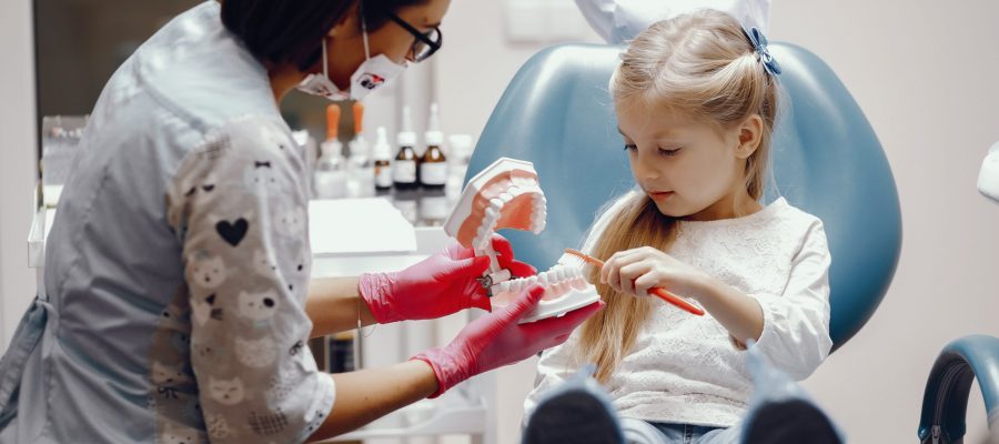 Little girl talking to the dendist. Child in the dentist's office. Woman in a uniform